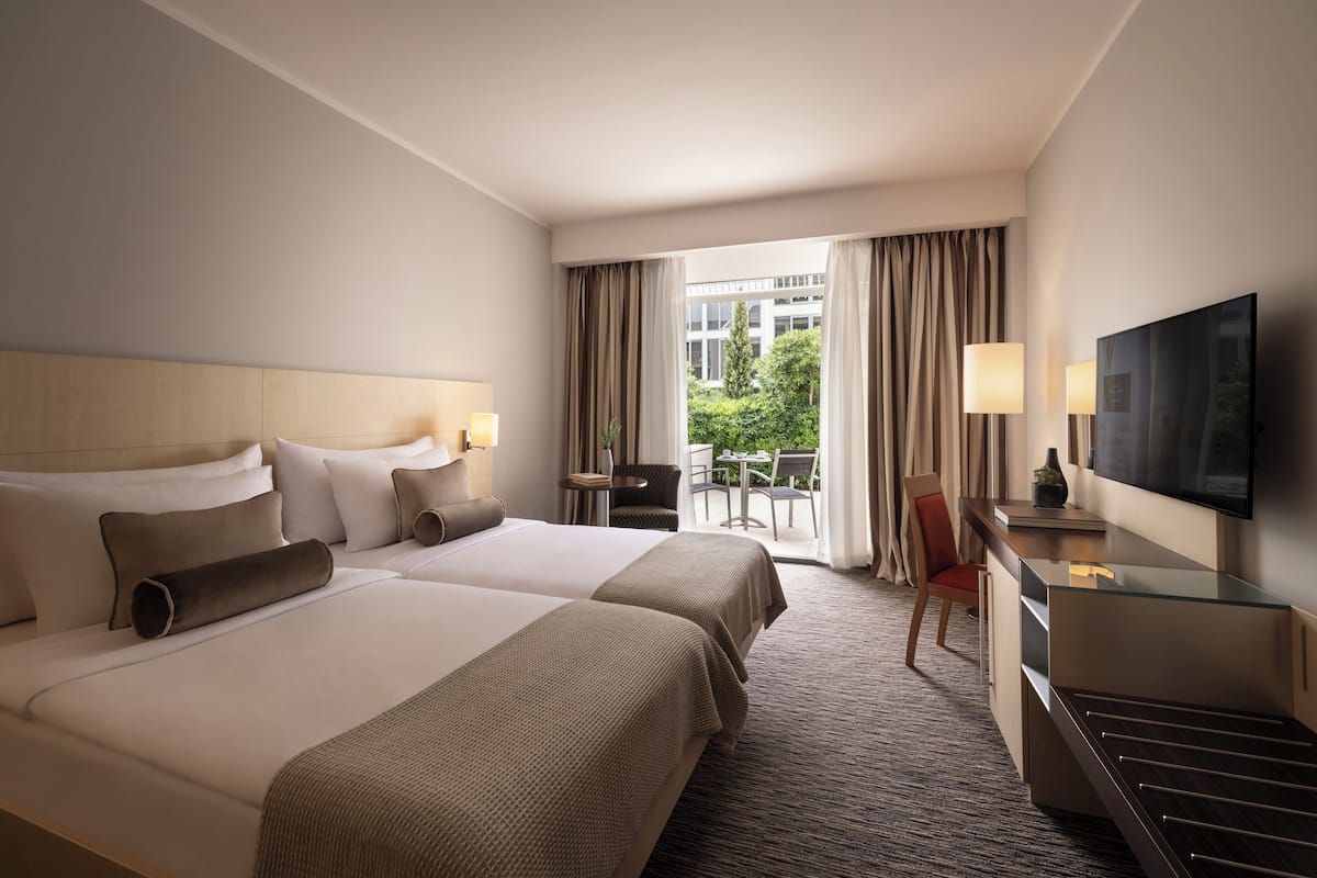 Habitación de hotel con dos camas, un escritorio, un televisor y un balcón con vistas al exterior.