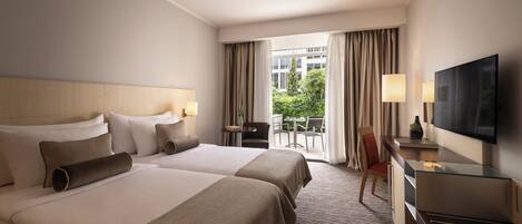 A hotel room with two beds, a desk, a TV, and a balcony with a view of the outdoors.