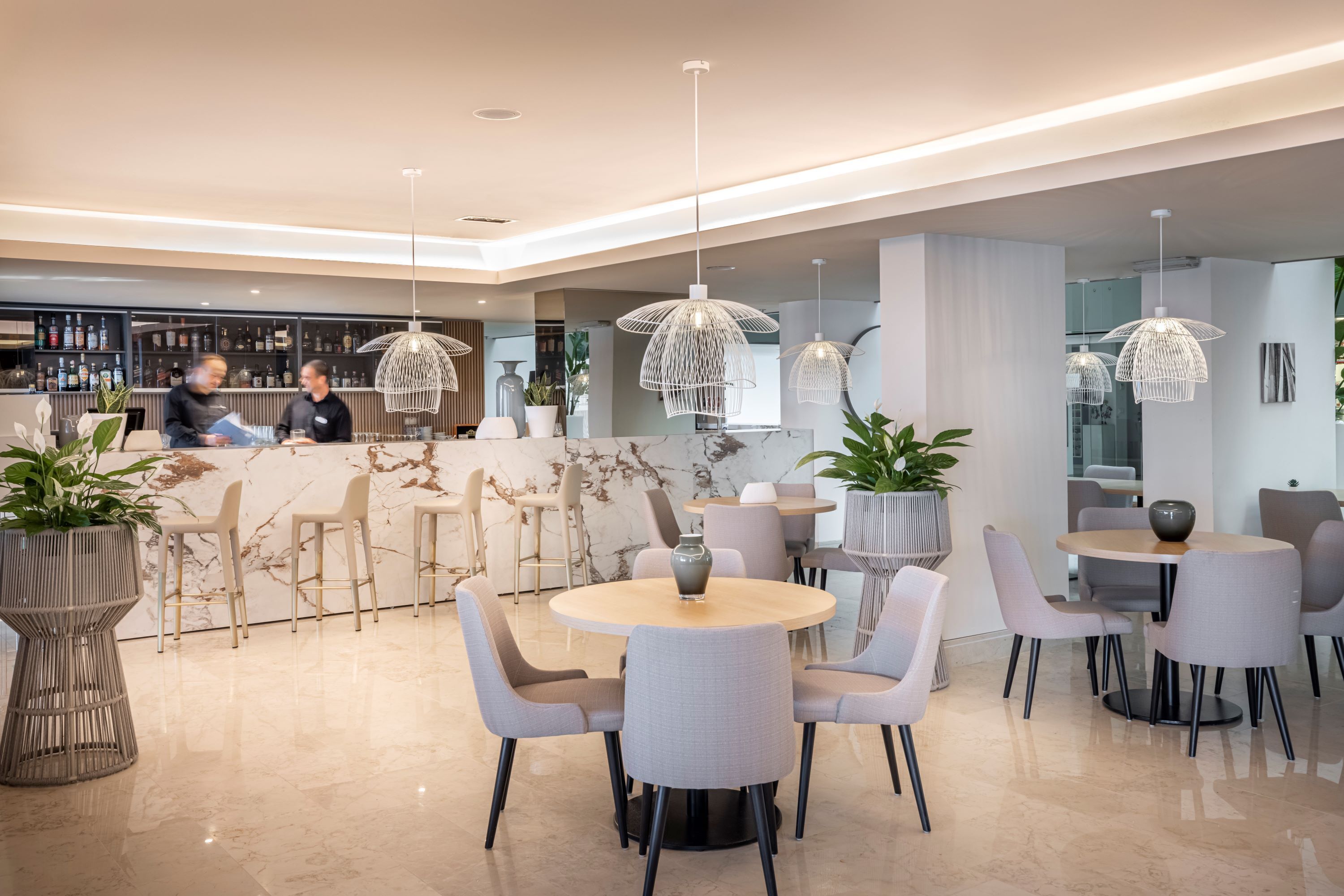 Eine moderne Hotelhalle mit runden Tischen, grauen Stühlen und einer Bar.