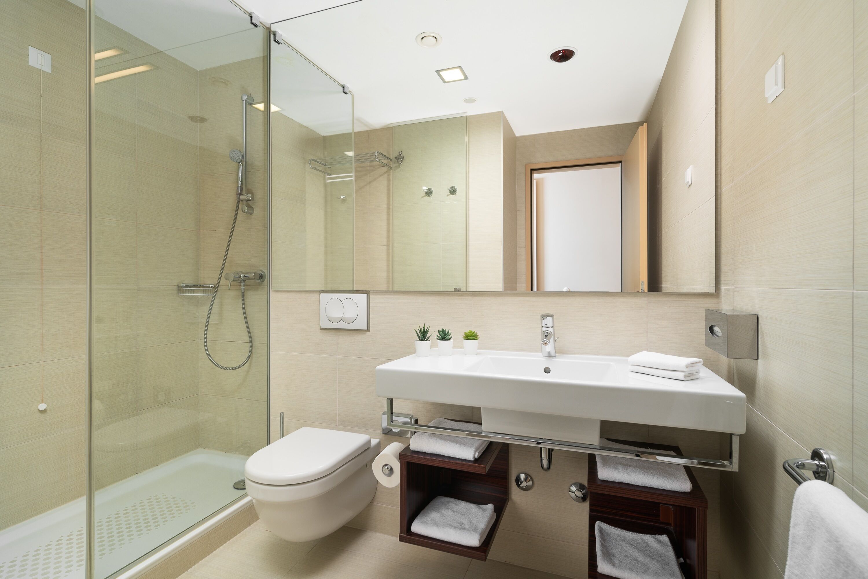A modern bathroom with a glass shower enclosure, a white sink with a mirror above, and a toilet.