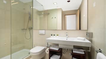 A modern bathroom with a glass shower enclosure, a white sink with a mirror above, and a toilet.
