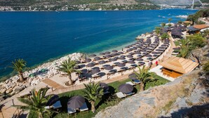 Un hotel frente al mar con zona de playa, sombrillas y vistas al océano y montañas.