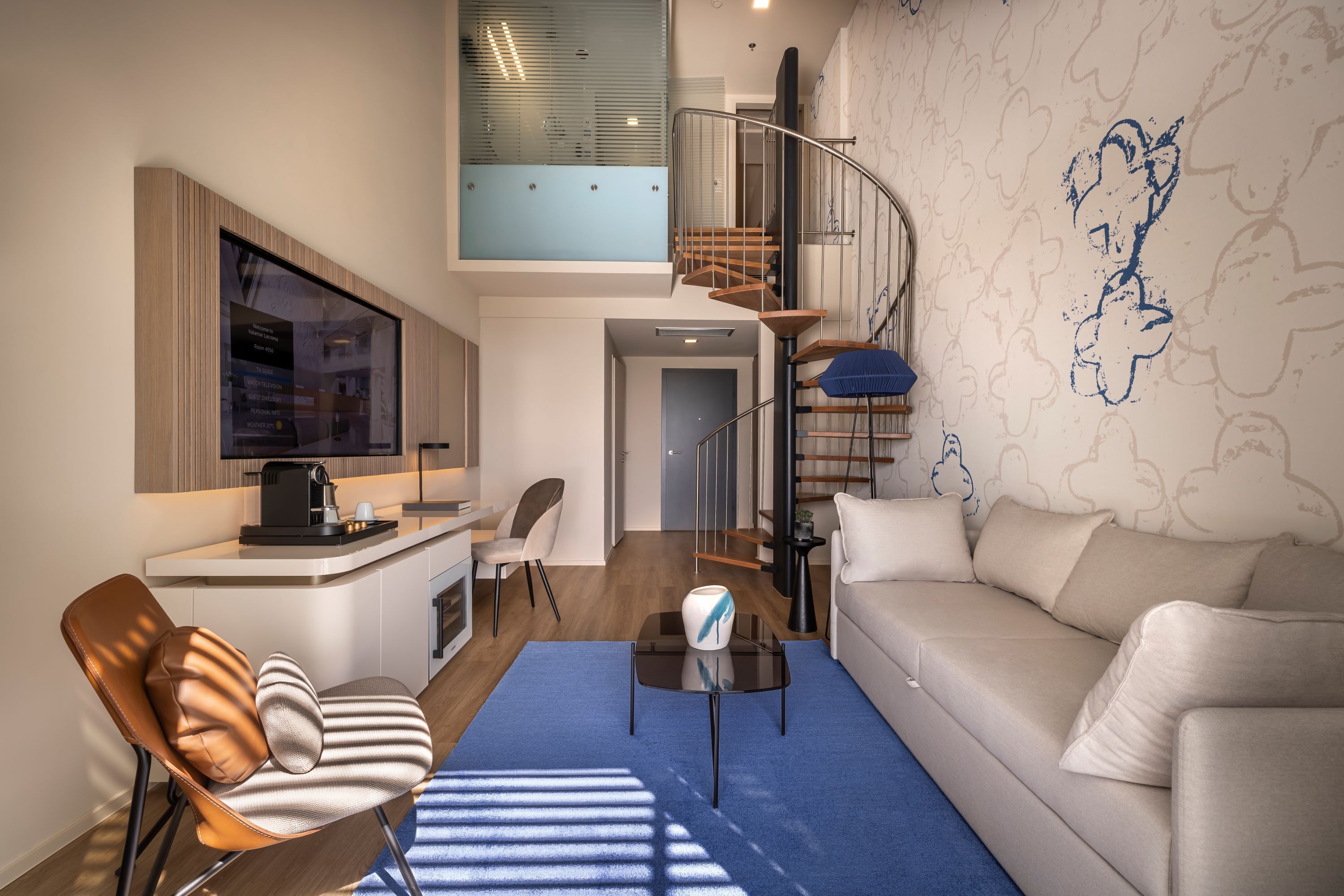 Una sala de estar moderna con un sofá, una mesa de centro y un sillón. Se ve una escalera que sube a un nivel superior.