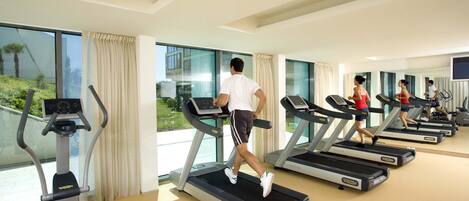 A gym with treadmills, a mirrored wall, and large windows with curtains.