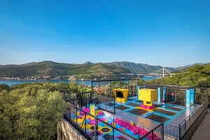 Parque de trampolins com estruturas coloridas, com montanhas e uma ponte ao fundo.