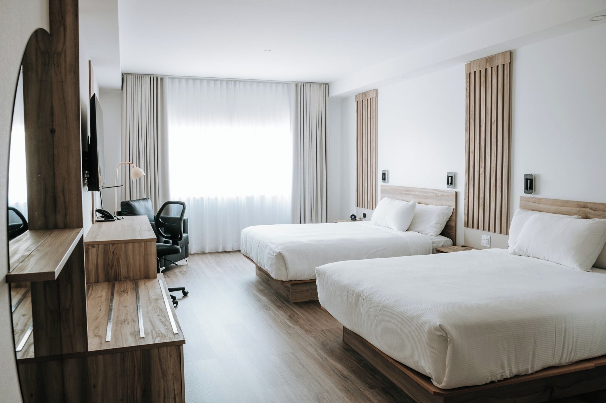 Habitación de hotel con dos camas, un escritorio, una silla y un televisor.
