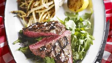 Un plato con bistec a la parrilla, vegetales verdes y un gajo de limón, con un cuchillo y sal al lado.