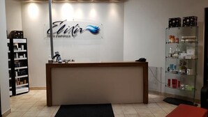 Zona de recepción con mostrador, señalización en la pared, estante con productos y un felpudo negro en el suelo.
