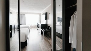 Una habitación de hotel con una cama, un escritorio, una silla, un espejo y un armario.