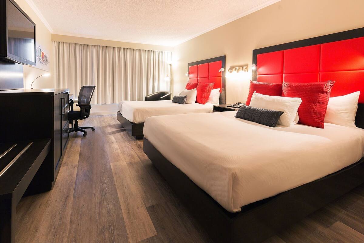 Una habitación de hotel con dos camas, un escritorio, una silla, un televisor y una cortina.