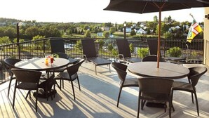 Una terraza con mesas y sillas redondas, un paraguas grande y vista a un barrio residencial.