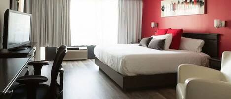 A hotel room with a bed, a desk with a chair, a television, and a red accent wall.