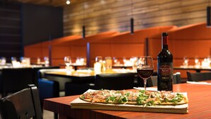 Un ambiente de restaurante con una mesa lista para comer, que incluye una pizza, una copa de vino y una botella de vino.