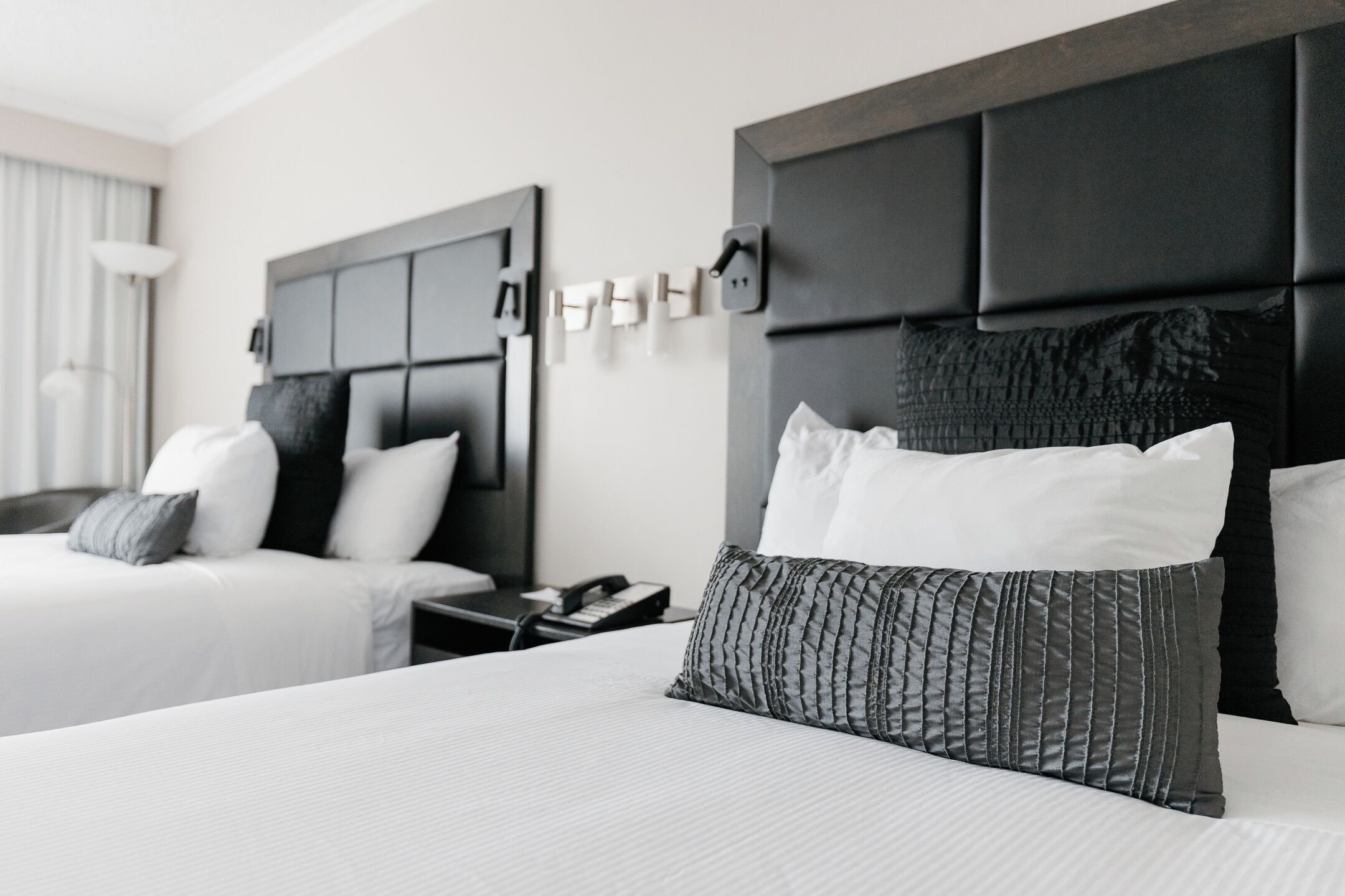 A hotel room with a large bed, a smaller bed, a nightstand with a phone, and a wall-mounted light fixture.