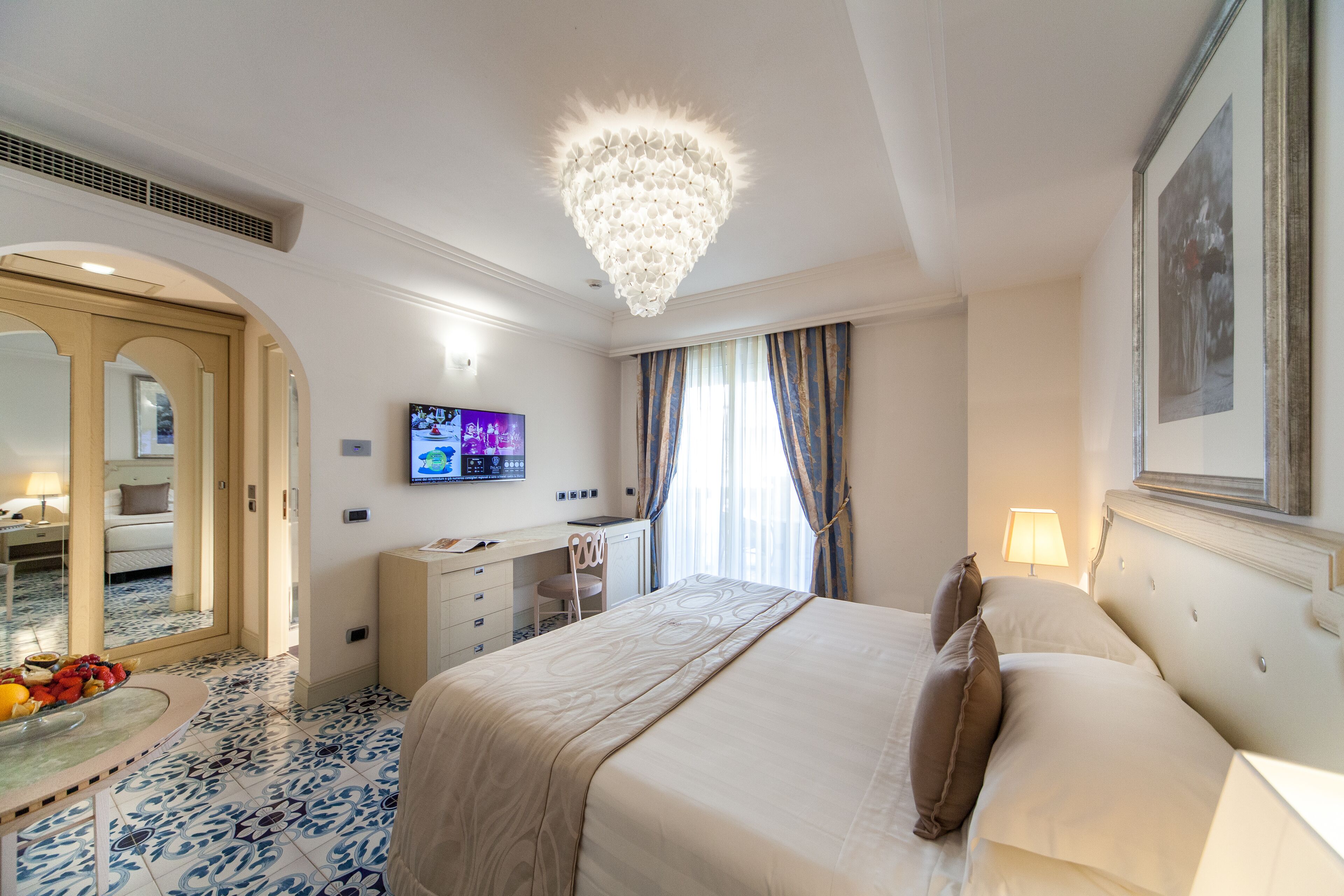 Una habitación de hotel con una cama grande, un escritorio con computadora, un televisor y un baño con espejo e inodoro.