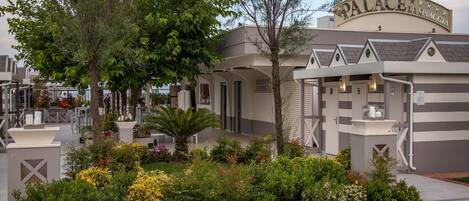 A hotel with a sign reading "PALACE LA SPIAGGIA" featuring a modern design with a garden area in front.