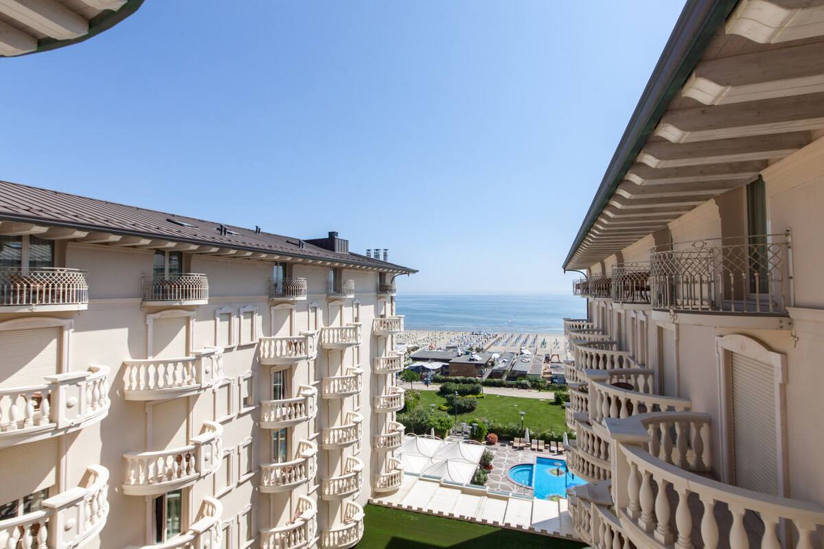 A high-rise hotel with multiple balconies, a swimming pool, and a view of the sea.