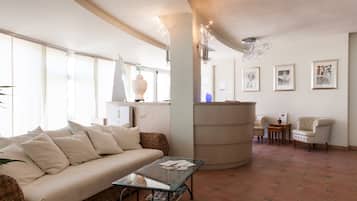 Una sala de estar con un sofá, una mesa de centro de vidrio, una silla de mimbre, una mesa redonda y una lámpara de pared.