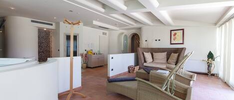 A spacious living area with a curved white reception desk, wicker furniture, and a large window providing natural light.