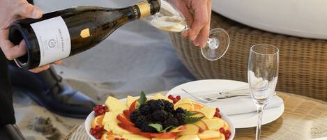 A person pouring champagne into a glass, a fruit platter on a table, and a wicker table setting with plates and cutlery.
