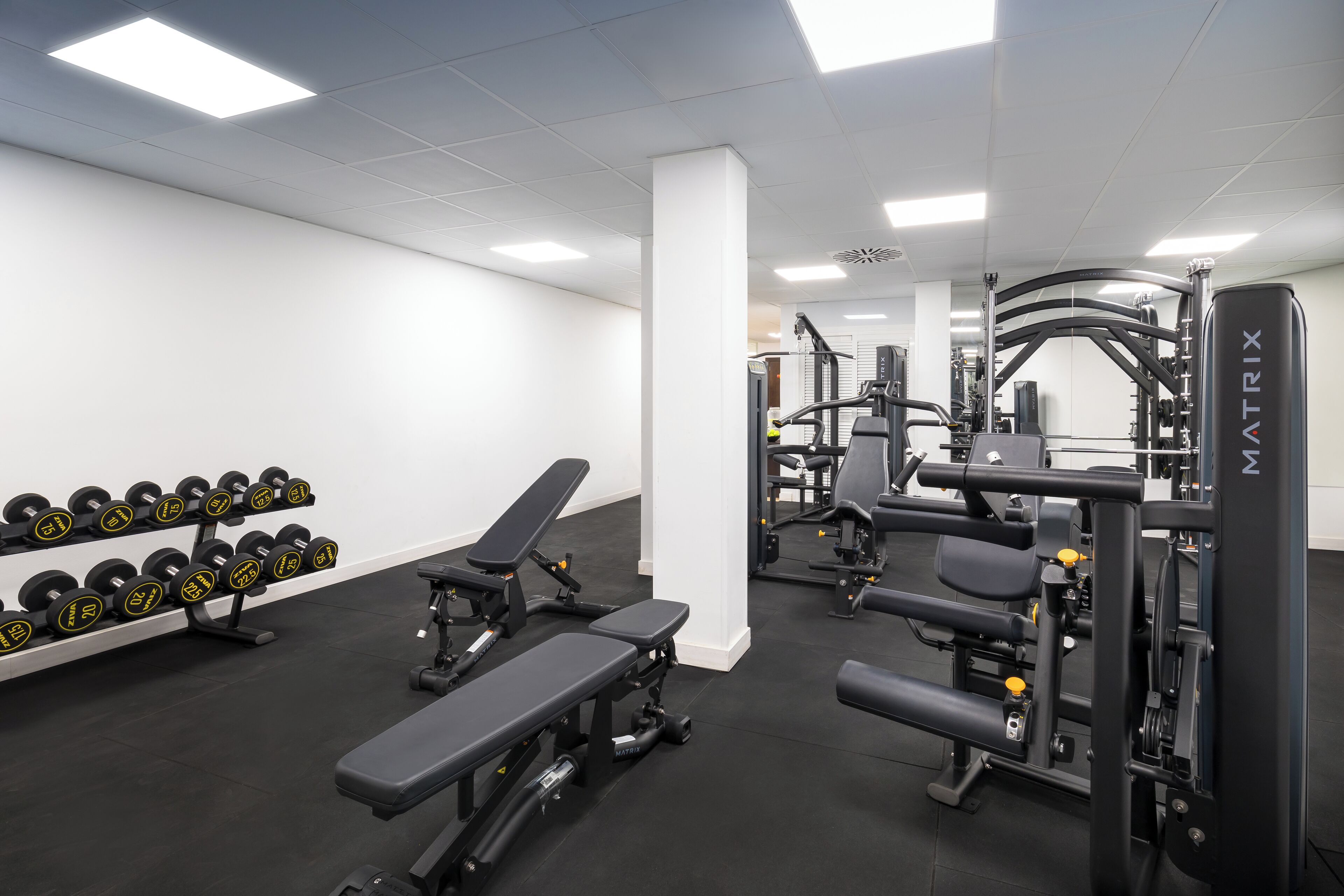 Un gimnasio con bancos, mancuernas y máquinas de pesas.