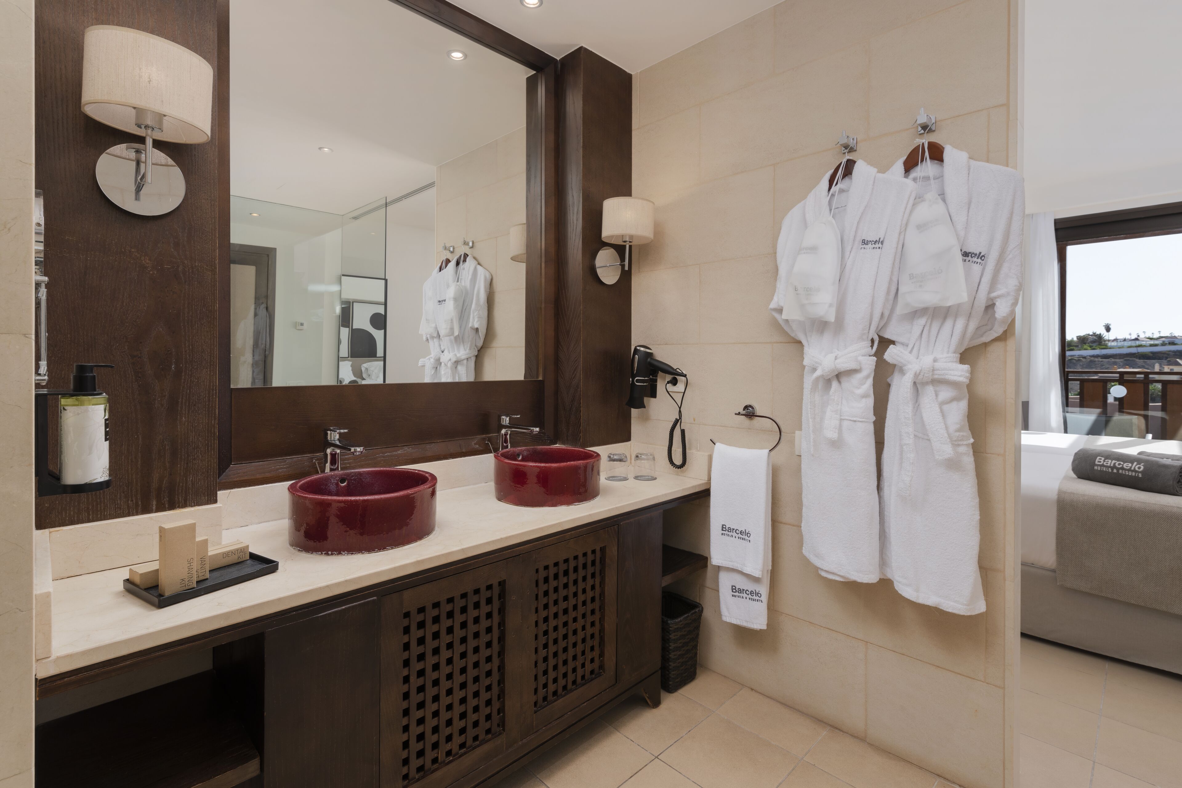 Un baño moderno con dos lavamanos, un espejo grande y un perchero con dos albornoces blancos.
