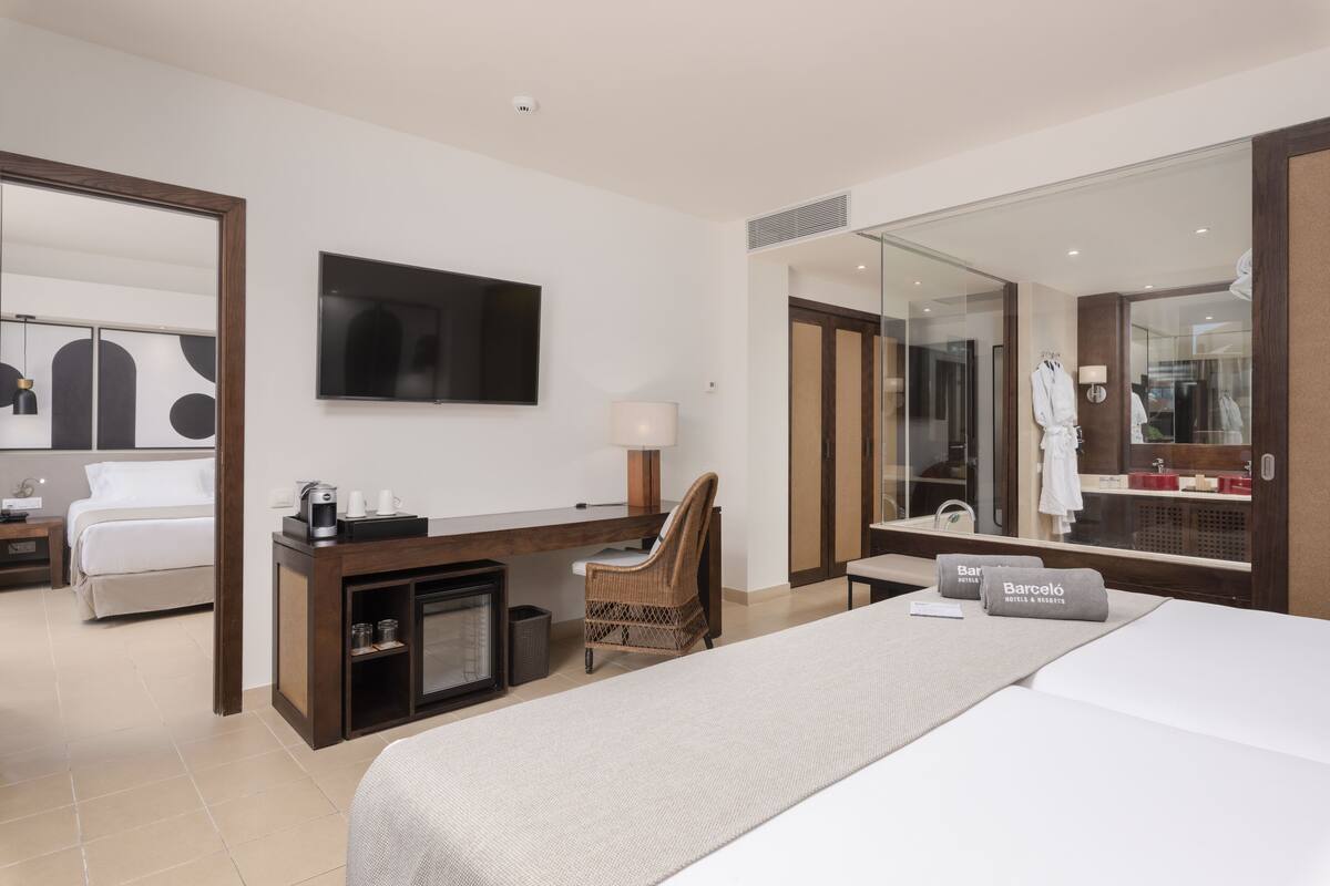 Ein Hotelzimmer mit Bett, Schreibtisch mit Stuhl, Fernseher, Spiegel und Minibar.