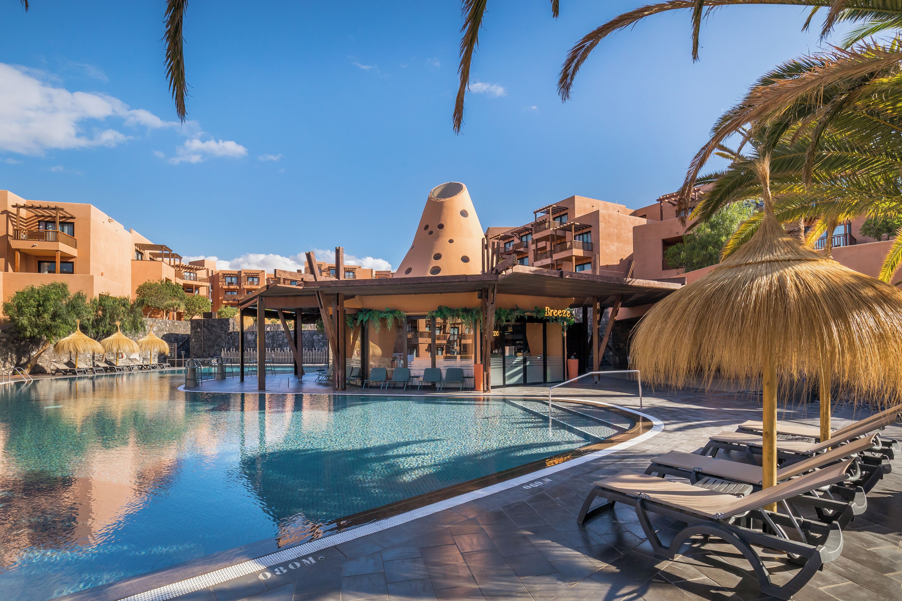 A swimming pool with lounge chairs, a thatched umbrella, and a unique conical building in the background.