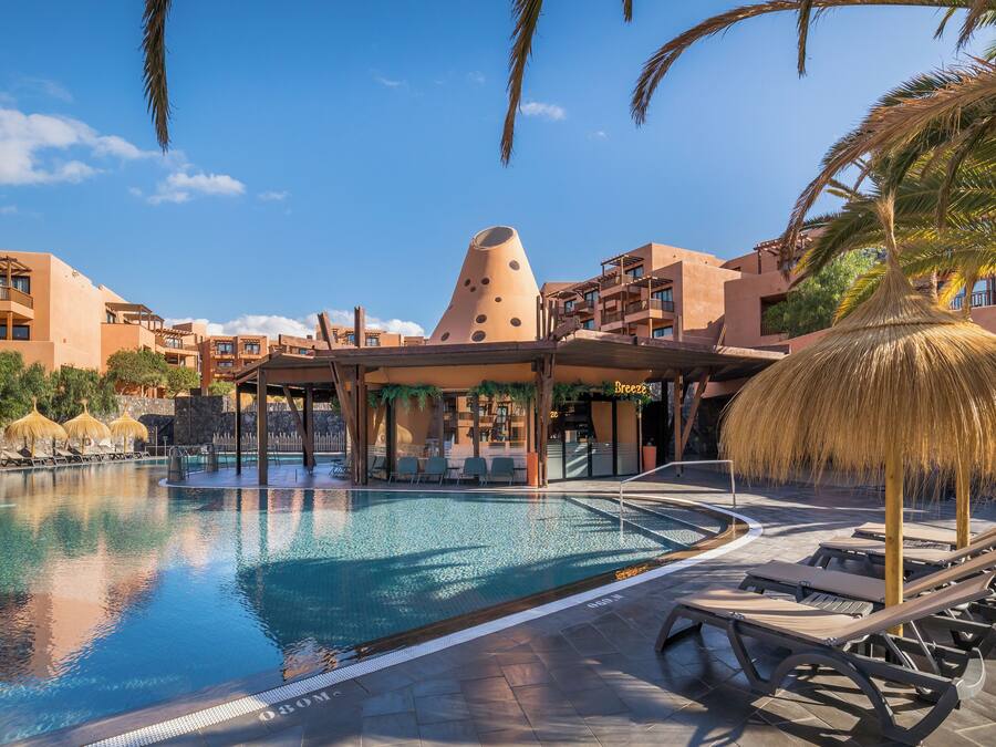A swimming pool with lounge chairs, a thatched umbrella, and a unique conical building in the background.