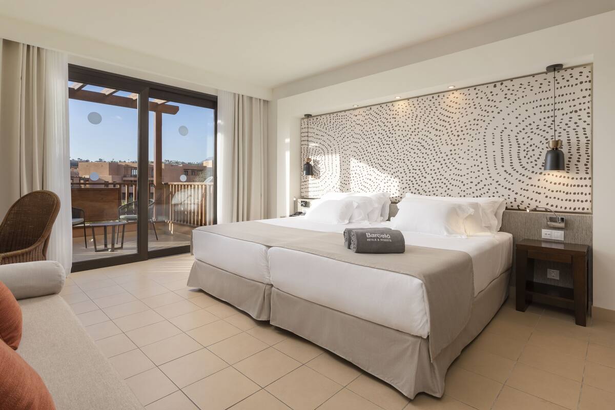Ein modernes Hotelzimmer mit einem großen Bett, einem Balkon mit Blick und einer Wandleuchte sowie einem kleinen Nachttisch.
