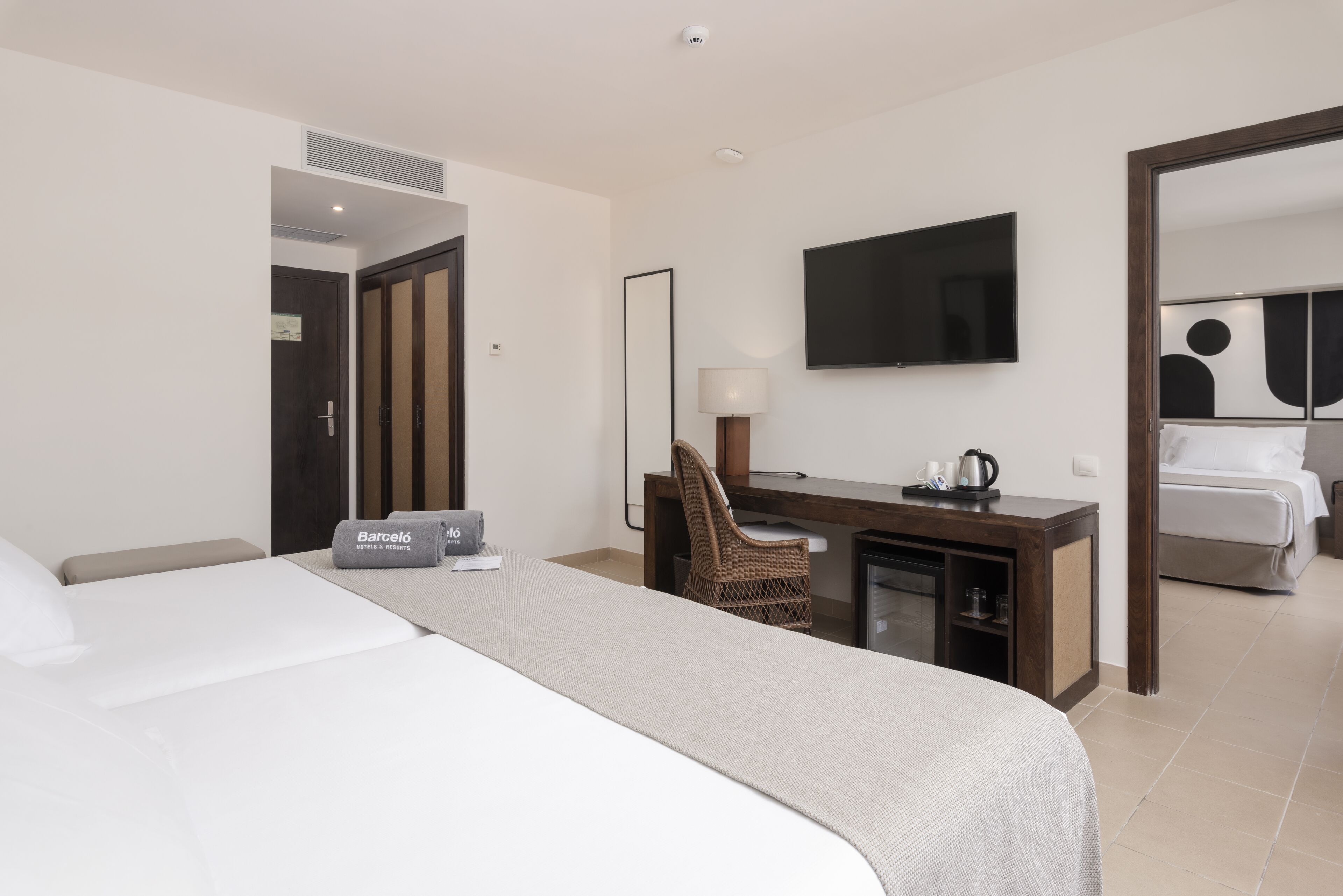 A hotel room with a large bed, a desk with a chair, a flat-screen TV, and a mirror.