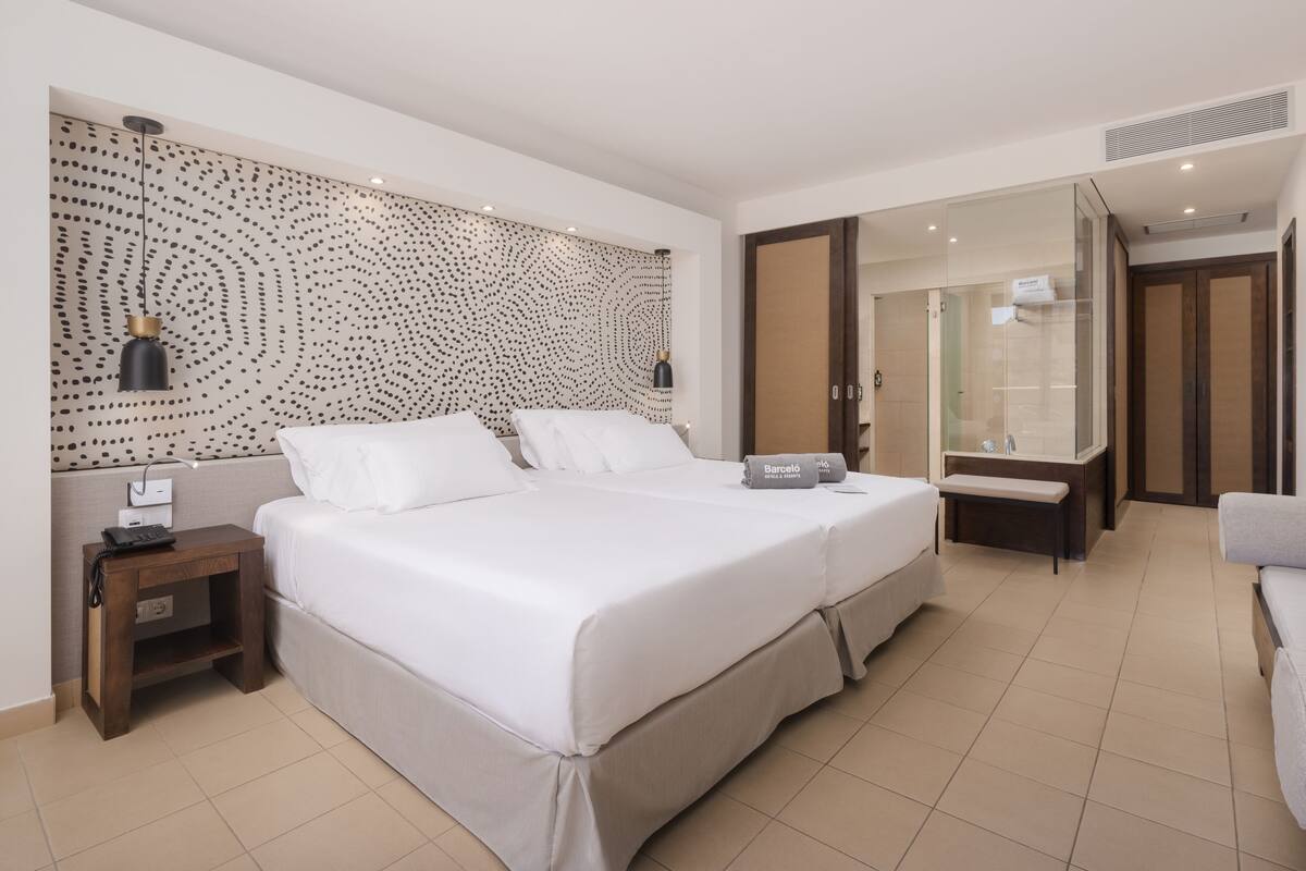 Ein Hotelzimmer mit einem großen Bett, einem Nachttisch mit Telefon, einem Spiegel und einem Badezimmer mit Duschkabine.