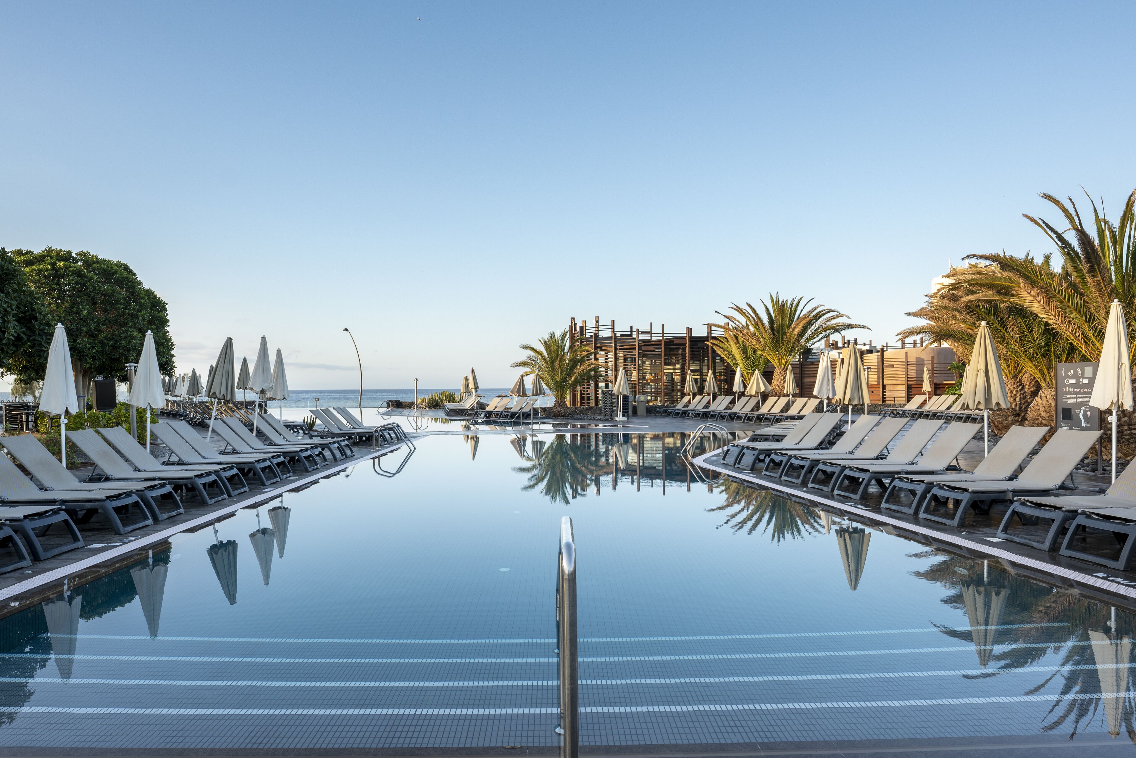 A poolside area with lounge chairs and umbrellas, a clear sky, and a view of the sea.