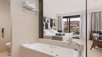 Ein modernes Badezimmer mit einer großen Badewanne, einer Toilette und einer Dusche. Im Spiegel ist ein Schlafzimmer mit einem Bett und einem Balkon zu sehen.