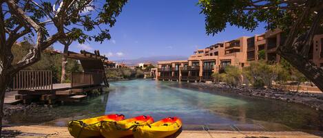 A river with kayaks, a wooden dock, and buildings in the background.