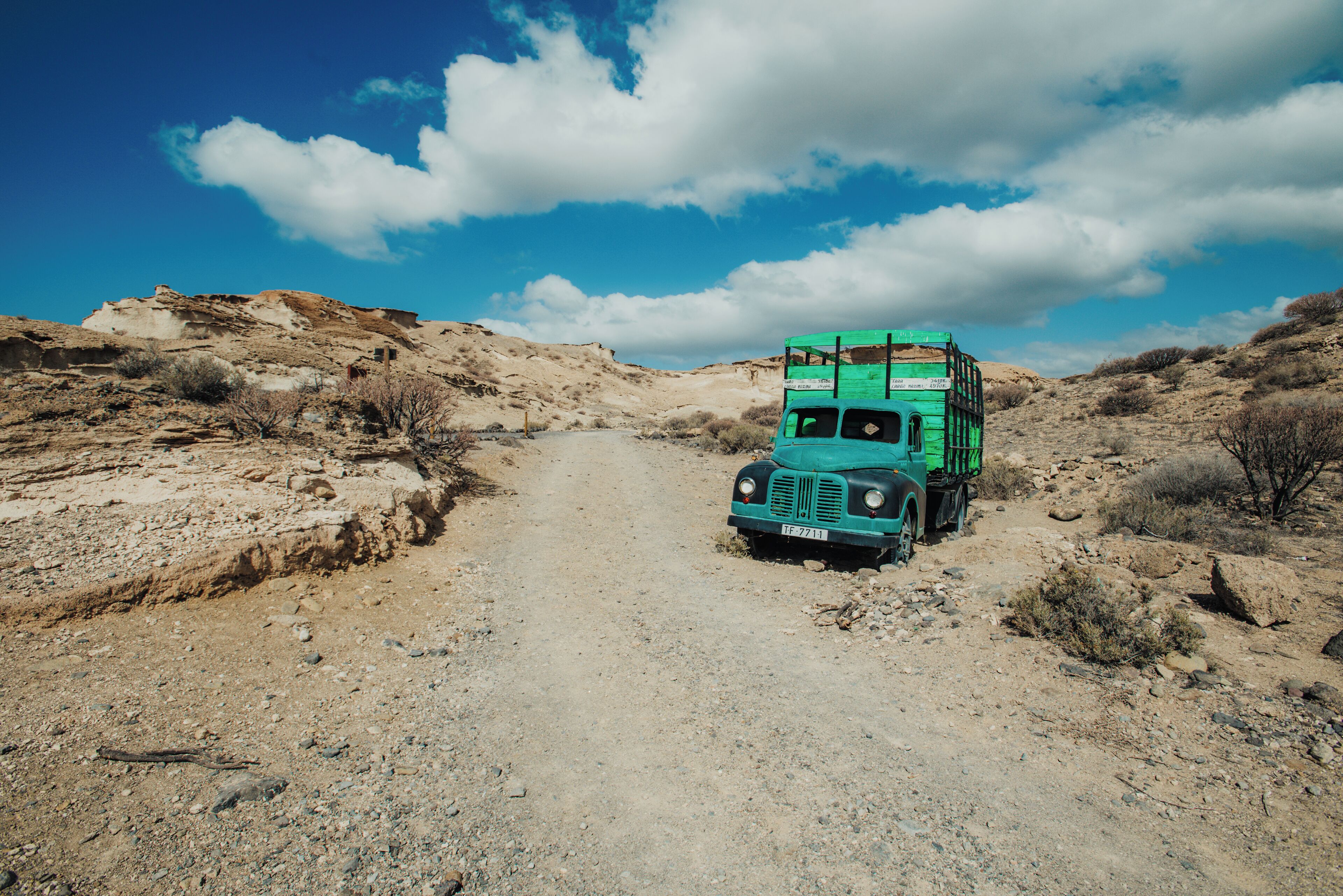 A green truck parked on a dirt road in a desert landscape.