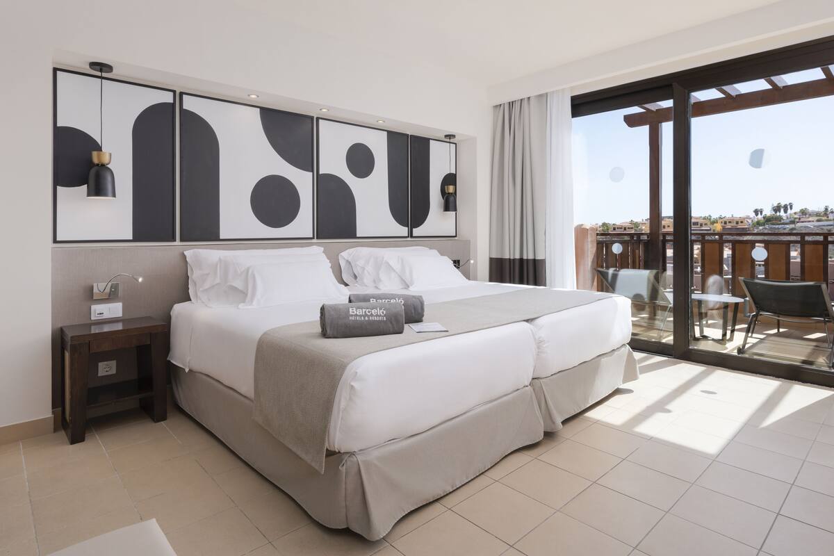 Ein modernes Hotelzimmer mit einem großen Bett, einem Nachttisch, einem Schreibtisch und einem Balkon mit Sitzgelegenheit.