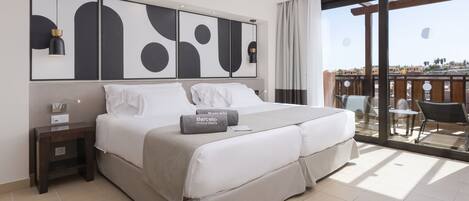 A modern hotel room with a large bed, a nightstand, a desk, and a balcony with outdoor seating.