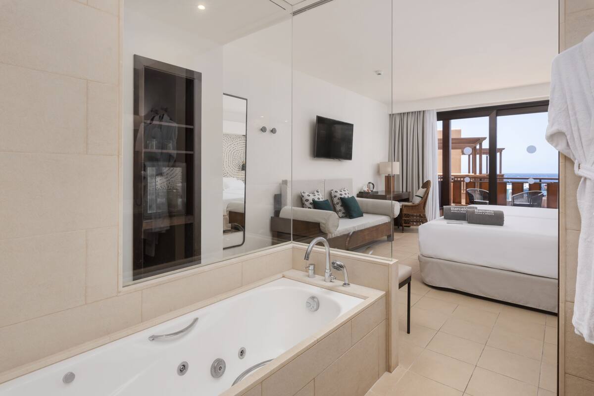 Ein modernes Hotelzimmer mit einer großen Badewanne, einem Sofa, einem Bett und einem Balkon mit Meerblick.