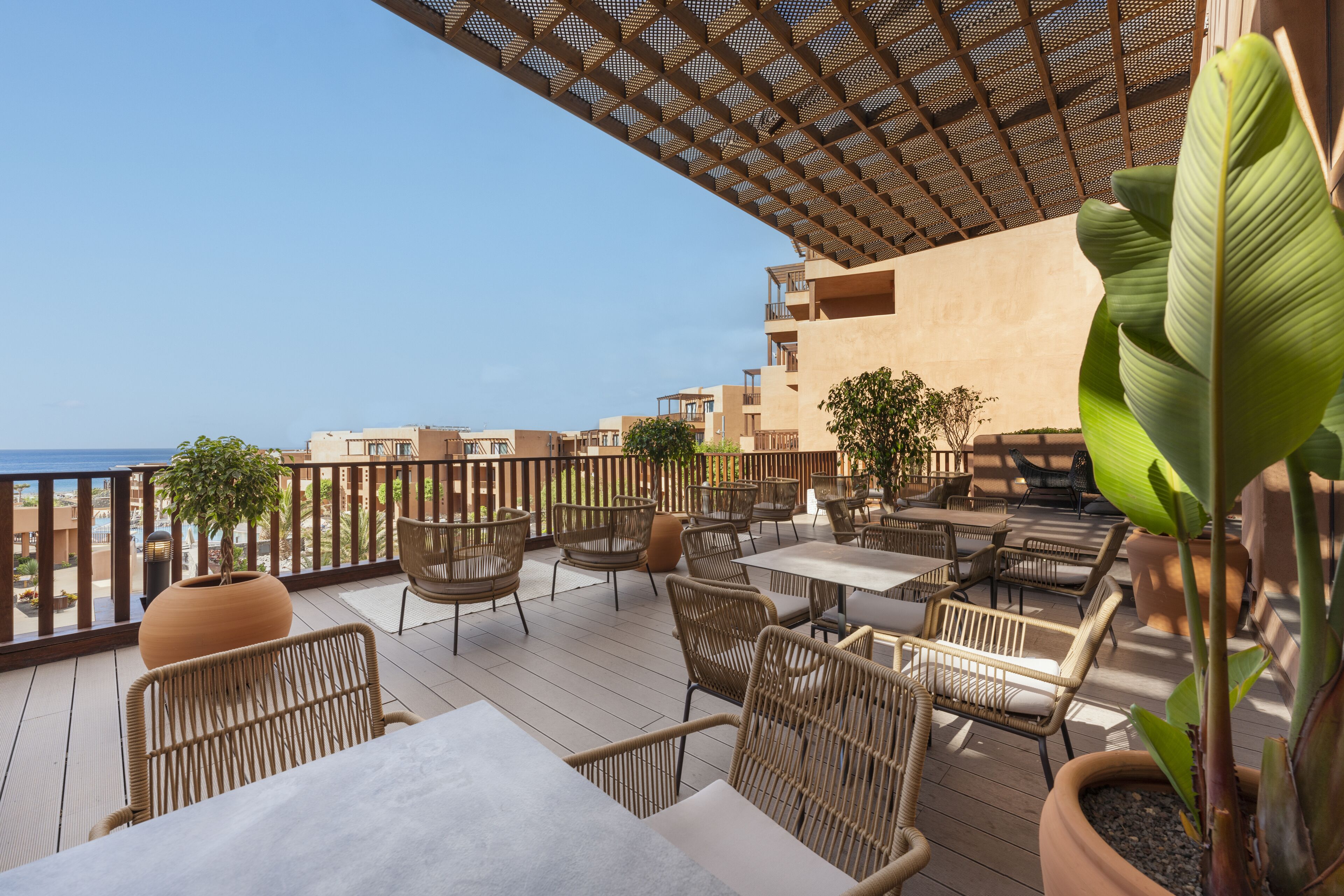 A terrace with wicker furniture, potted plants, and a view of the sea.
