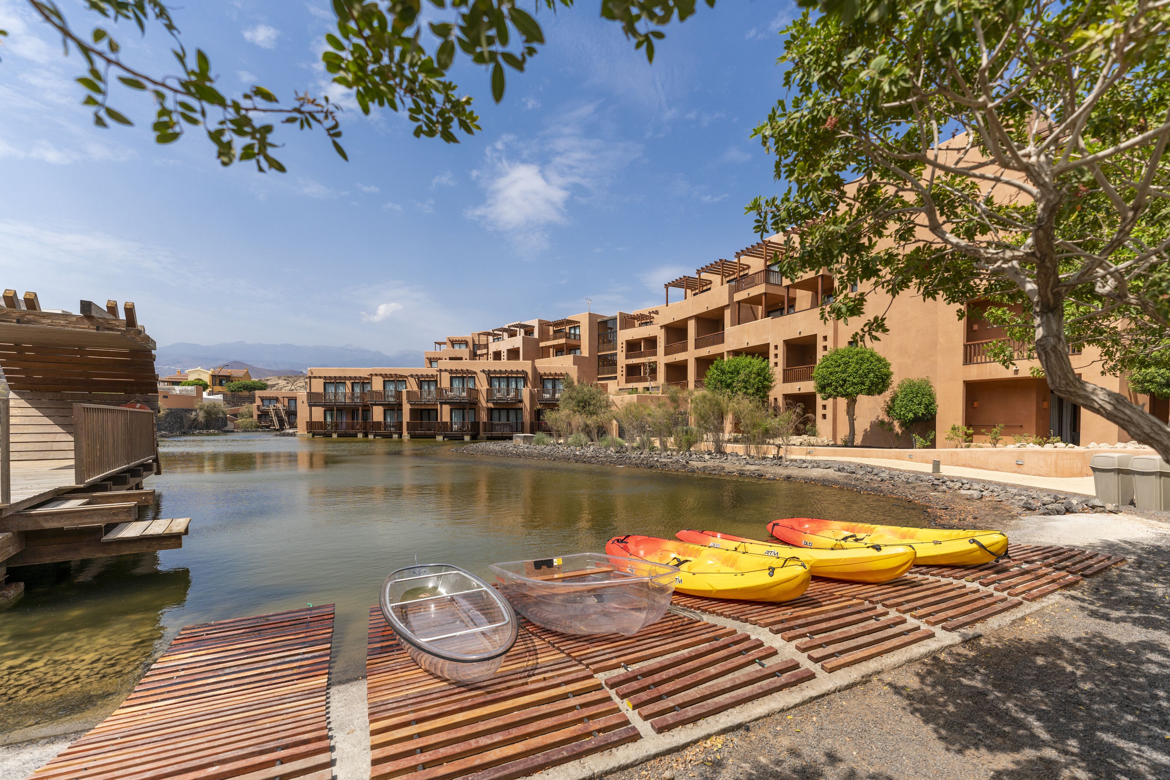 A riverside view with a dock, kayaks, and a building with balconies.