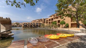 A riverside view with a dock, kayaks, and a building with balconies.