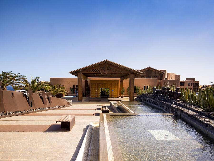 A resort with a pool, palm trees, and a building with a covered entrance.
