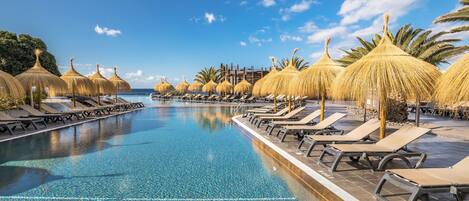 A swimming pool with lounge chairs and thatched umbrellas, surrounded by palm trees.
