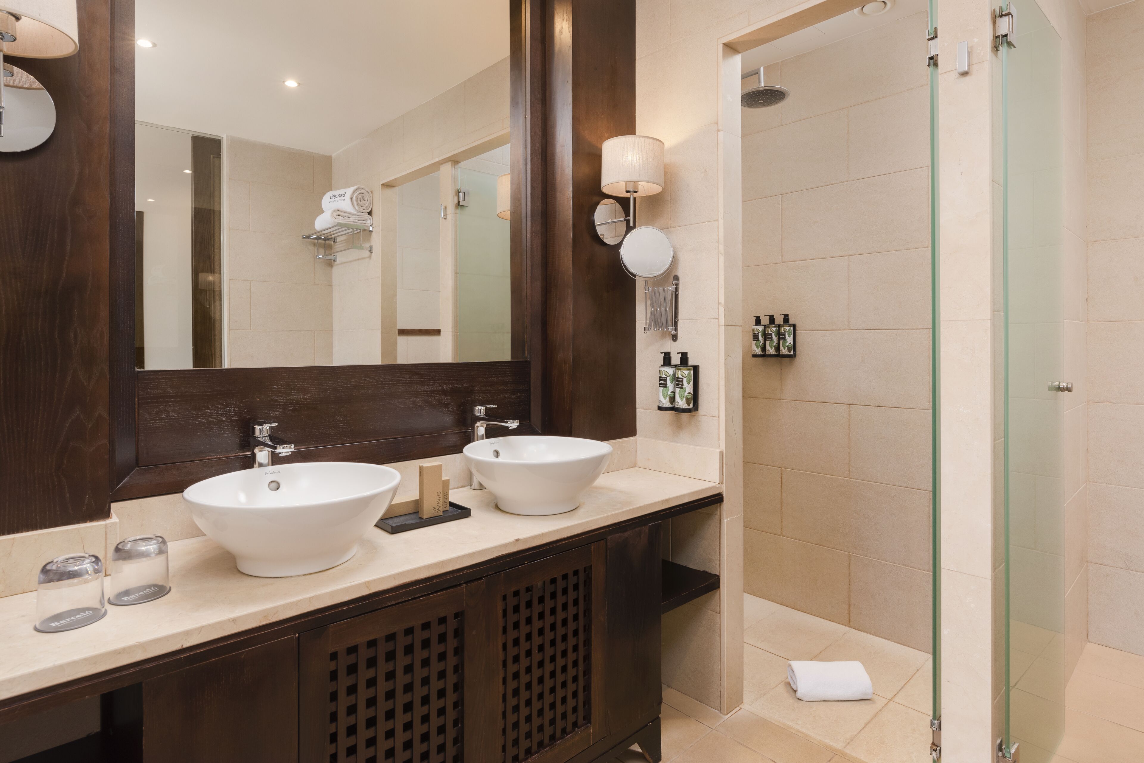 Un baño moderno con dos lavamanos, un espejo grande y una ducha con cerramiento de vidrio.