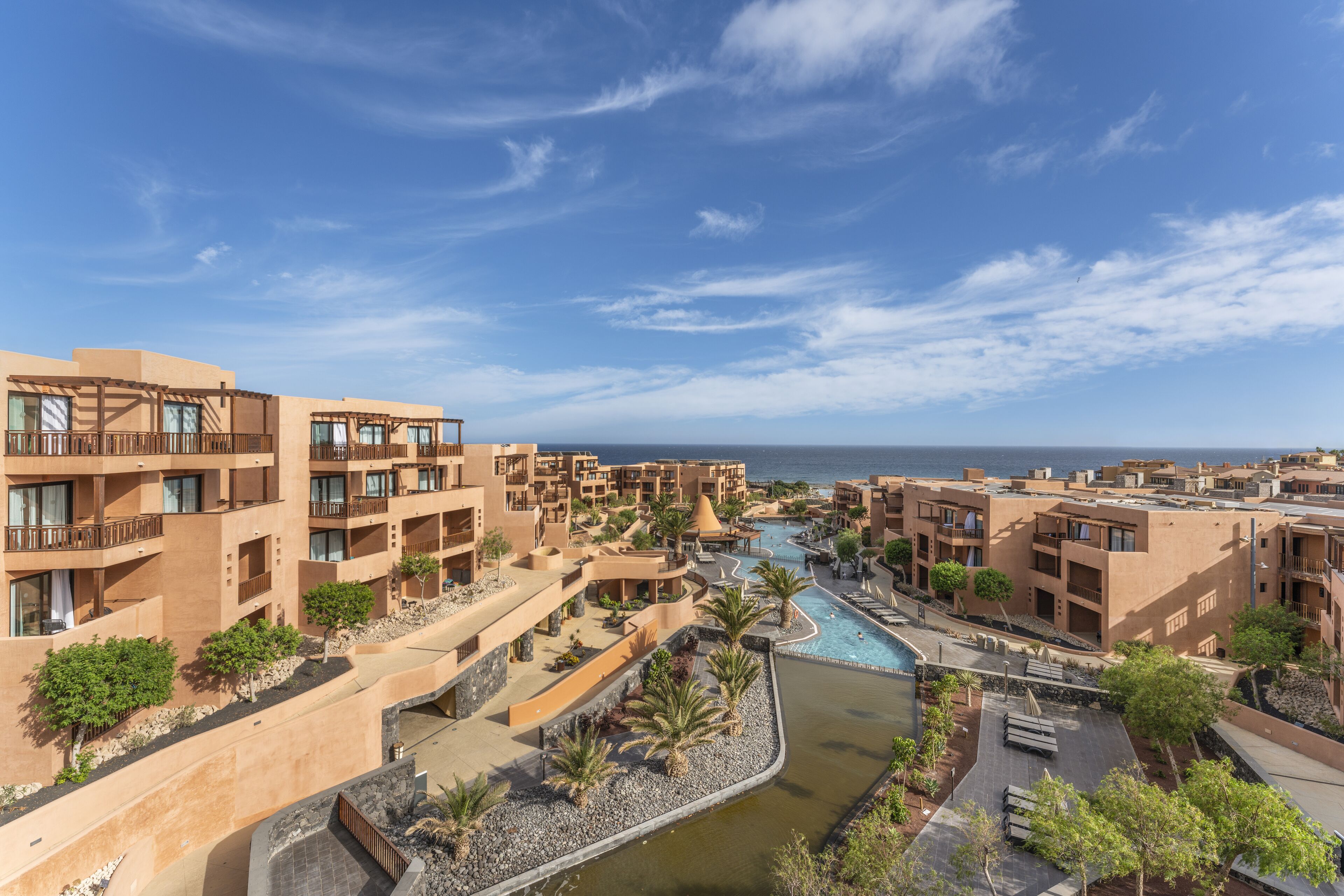 A resort with multiple buildings, a central pool, and a view of the sea.
