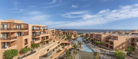 A resort with multiple buildings, a central pool, and a view of the sea.
