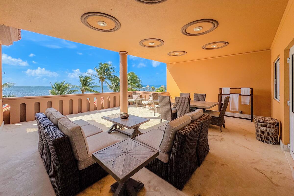 A sunlit outdoor seating area with wicker furniture, a view of the ocean, and a ceiling with circular light fixtures.