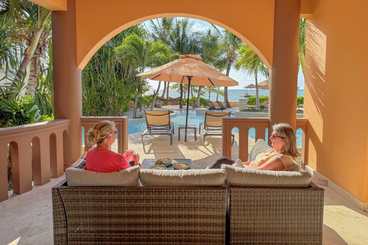 A covered outdoor seating area with wicker furniture, a pool, and a view of the ocean.