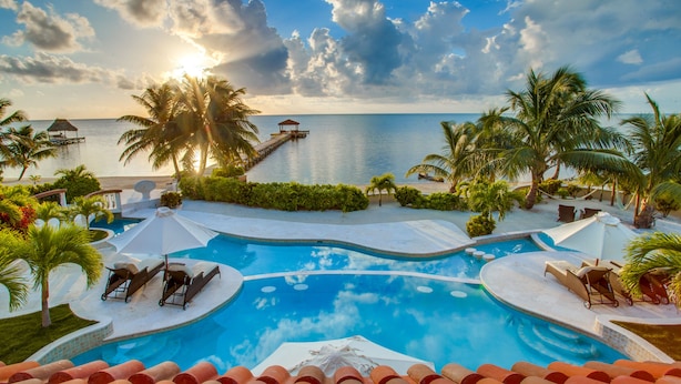 Una piscina de resort con vistas al océano, palmeras y un muelle.